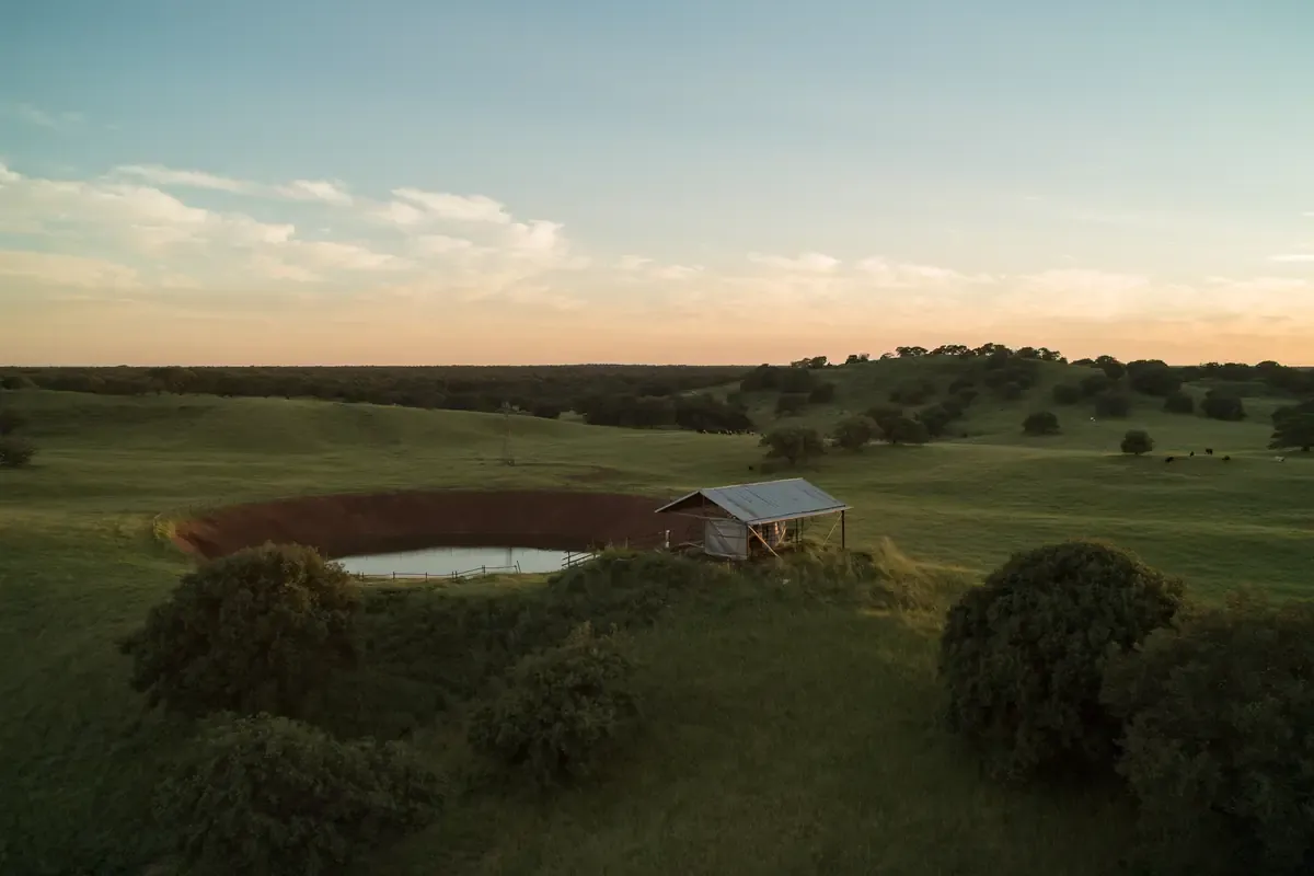 Rolling pasture with a stock tank and a small metal shed in Karnes County, Texas