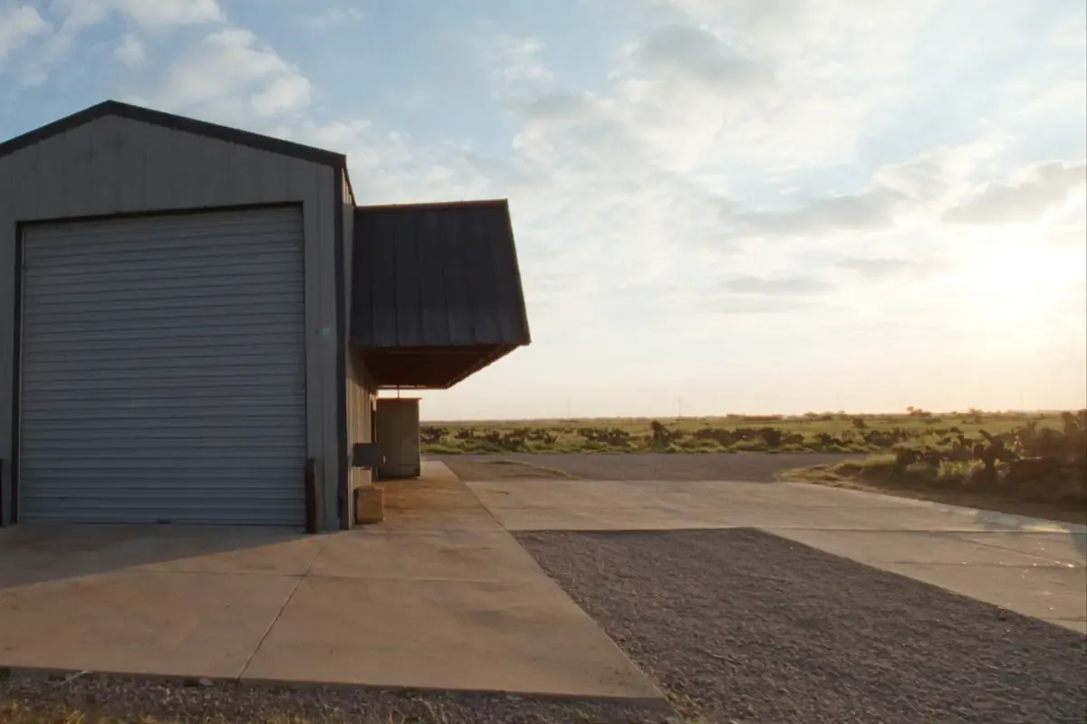 Gray metal shop building with a roll-up door on a concrete apron in South Texas