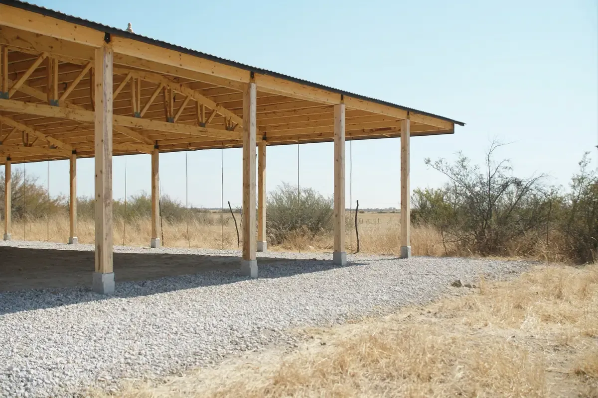 Open post frame pole barn with wood posts and trusses on gravel in South Texas