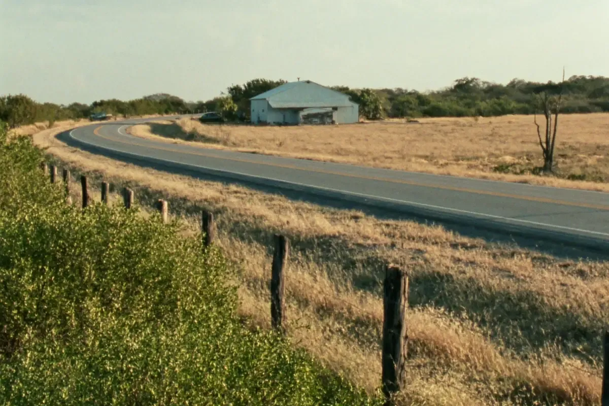 Two lane rural road curving past a metal building in the brush country south of San Antonio, Texas