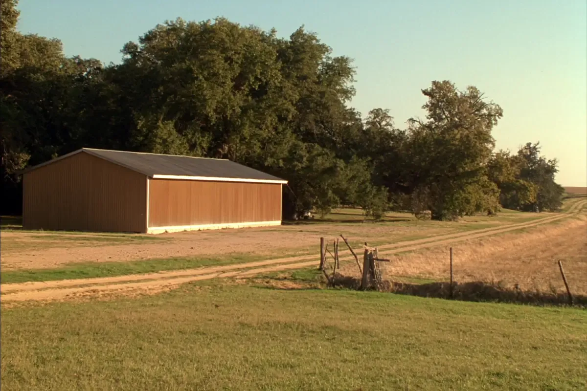 Tan gable roofed metal building among live oaks in Wilson County, Texas